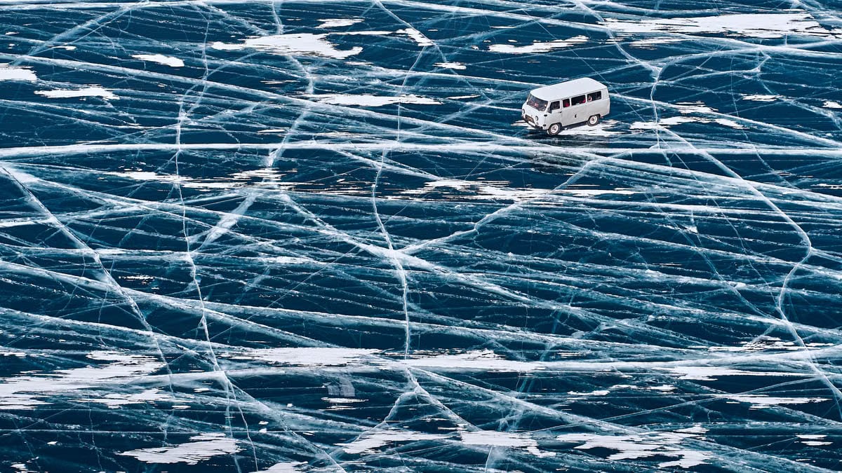A van driving across the icy surface of Lake Baikal with intricate ice patterns.